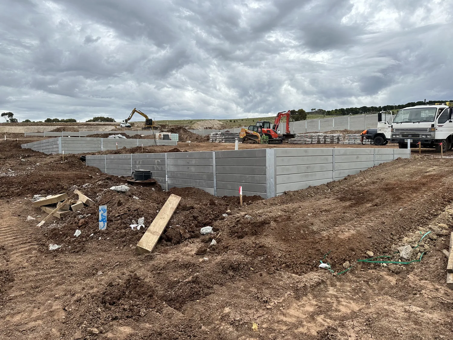 Large commercial grey sleeper retaining wall with machines on site